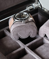 A Grove Watch Box Pillows - X-Small - Brown by TAWBURY, featuring a sleek design and spacious compartments ideal for watch collectors, elegantly showcases a black-dial wristwatch resting on its suede cushion.